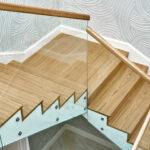 Sicht von oben auf eine Holztreppe mit Glasgeländer und Holzhandlauf