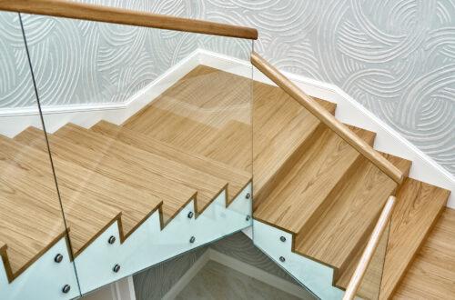 Sicht von oben auf eine Holztreppe mit Glasgeländer und Holzhandlauf