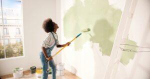 Junge Frau malt die Wand mit Walzenbürste beim Renovieren der Wohnung