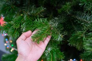 Hand, die das Blatt (die Nadeln) eines künstlichen Weihnachtsbaums berührt. 