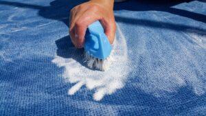 Die Hand einer Frau wäscht den Teppich mit einer Bürste. 